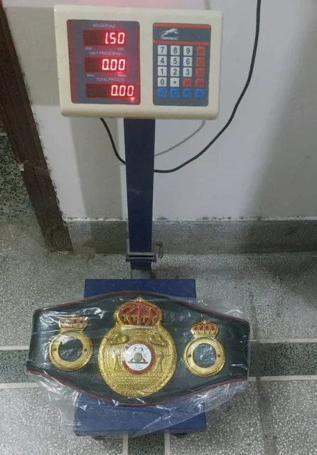 Finished championship belt on a digital scale showing its weight