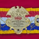 Finished boxing championship belt laid flat on a workbench with its full 48 inch strap visible